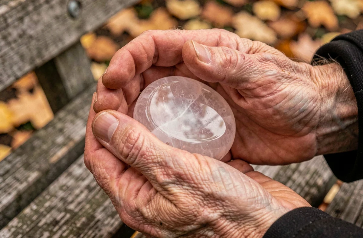 Gros plan de mains tenant une pierre de quartz rose worrying stone sur un banc de parc en automne, moment de pleine conscience